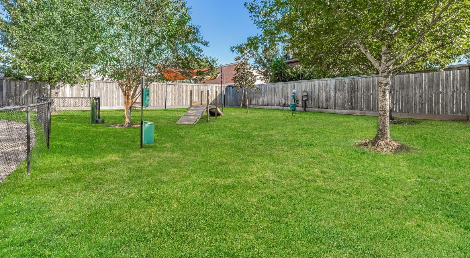 We welcome all your furry friends a fenced in dog park with trees and grass